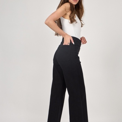 Mulher com top branco, calças pretas largas e sapatos brancos num fundo branco