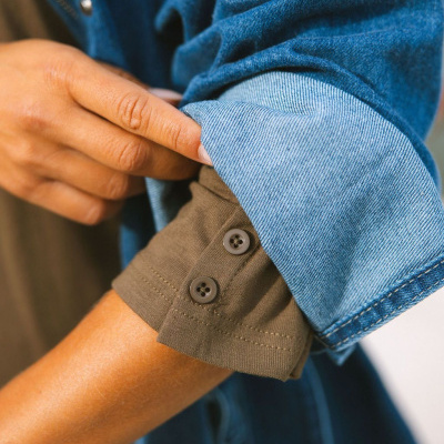 Manga de camisa castanha com botões e jaqueta de ganga azul clara enrolada na manga.