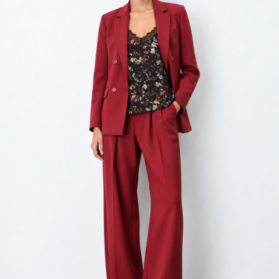 Mulher com blazer vermelho escuro, calças largas, top floral preto com renda e sapatos vermelhos escuros.