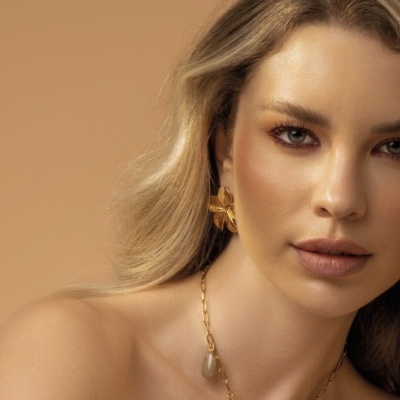 Mulher com brincos e colar dourados com pedras naturais, fundo bege