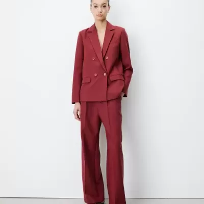 Mulher veste conjunto feminino vermelho escuro com blazer de botões duplos e calças largas, sapatos combinando, fundo branco.