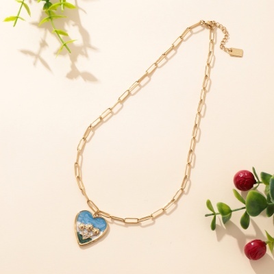 Colar dourado com pendente de coração azul e flores douradas.