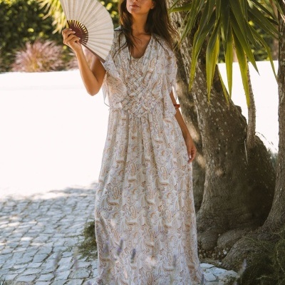 Vestido comprido leve com padrão paisley em tons neutros, mulher com leque em ambiente exterior