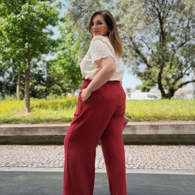 Mulher com camisa branca rendada manga curta e calças largas vermelhas ao ar livre