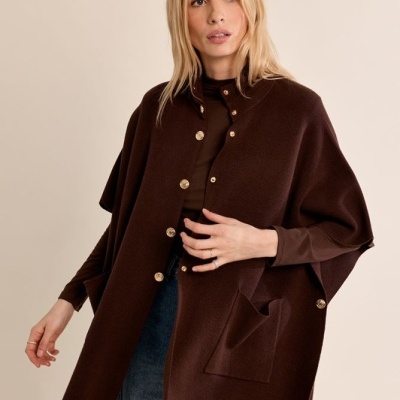 Mulher com capa castanha escura com botões dourados e jeans azuis