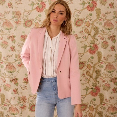 Mulher com blazer rosa, camisa branca e jeans azul claro em fundo floral.