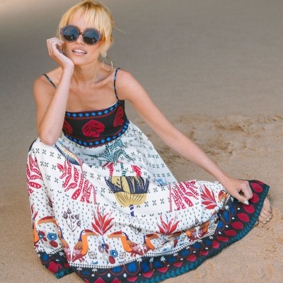 Vestido longo com estampa tropical colorida numa mulher sentada na praia.