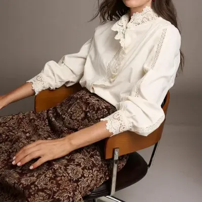 Mulher sentada numa cadeira com blusa branca com renda e saia castanha com padrão floral