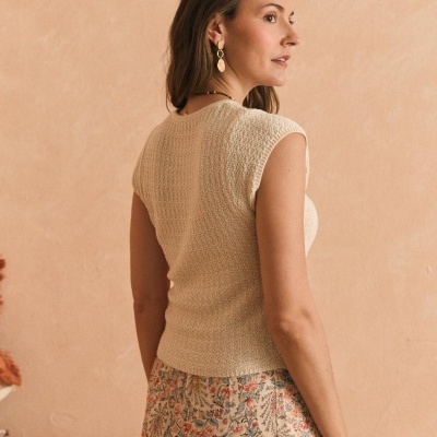 Mulher de costas com camisola de malha bege e saia com padrão floral num fundo pêssego.