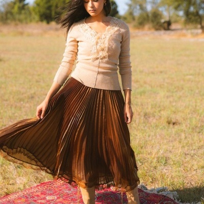 Mulher vestida com camisola bege e saia plissada castanha com botas bege em tapete vermelho no campo