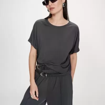 Mulher com óculos de sol pretos, brincos prateados, t-shirt e calças cinza escuras com cinto preto