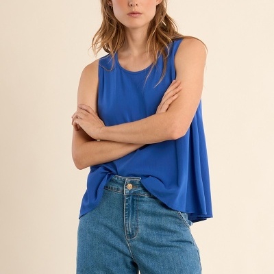 Mulher com camisola azul e calças de ganga azul claro com fundo bege.