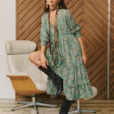 Vestido verde com padrão paisley e botas pretas usadas por mulher sentada.