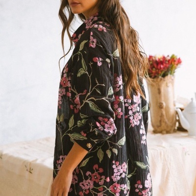 Camisa preta com bordados florais rosa e folhas verdes usada por mulher com cabelo castanho longo