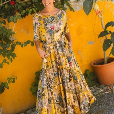 Vestido longo floral amarelo com bolsos e cinto em cenário exterior com parede amarela