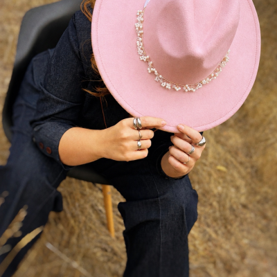 Pessoa sentada a segurar chapéu rosa com decoração de pérolas no exterior.