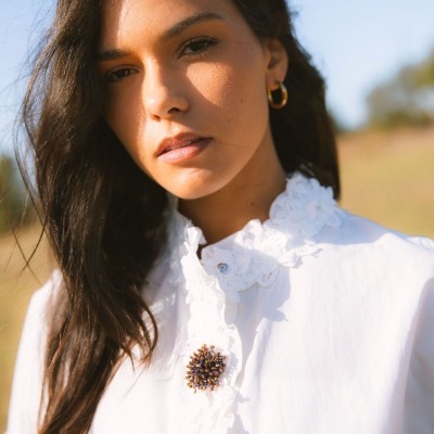 Mulher com camisa branca rendada e botões coloridos ao ar livre