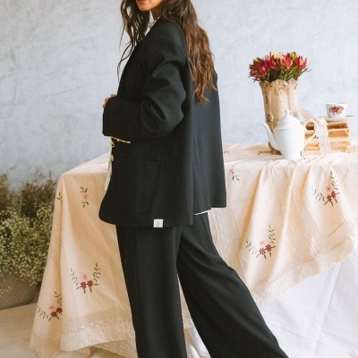 Mulher com blazer e calças pretas em ambiente interior com mesa decorada