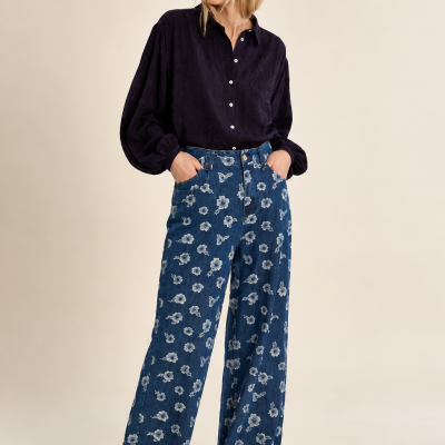 Mulher a usar calças jeans largas com padrão de flores e camisa escura com botões brancos
