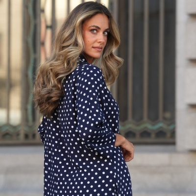 Vestido azul escuro com bolinhas brancas usado por mulher com cabelo loiro ondulado