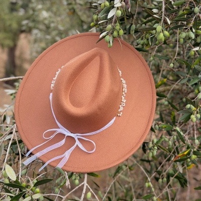Chapéu castanho de feltro com fita branca e pérolas pendurado em ramo de oliveira