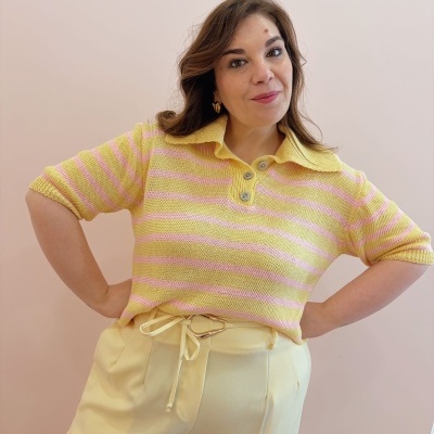 Mulher a vestir camisola de malha riscada amarelo e rosa com calças amarelas e cinto de corda