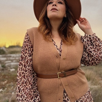 Mulher com colete castanho, vestido estampado animal print e chapéu castanho