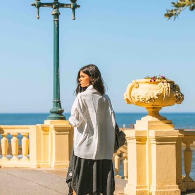 Mulher com camisa branca e saia cinza junto ao mar numa esplanada amarela