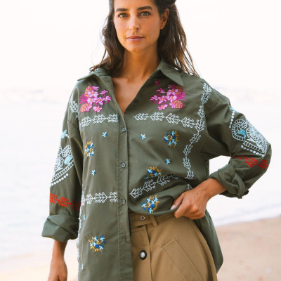 Camisa verde bordada com motivos florais coloridos usada com saia bege junto à praia