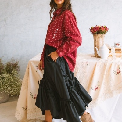 Mulher com camisa vermelha de bolinhas, saia preta com babados e botas castanhas em ambiente com mesa decorada