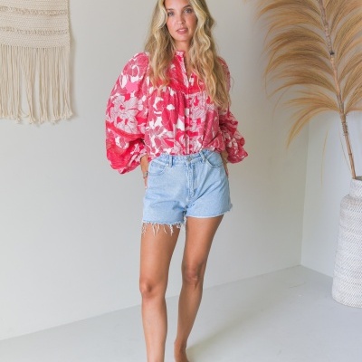 Mulher com blusa floral vermelha e branca e calções de ganga com decoração natural ao fundo