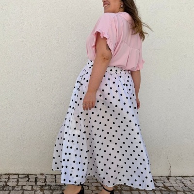 Mulher com blusa rosa e saia branca de bolinhas pretas em parede branca