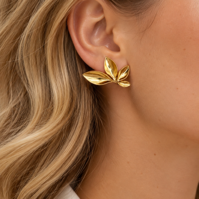 Brinco dourado em forma de folhas em orelha feminina com cabelo loiro ondulado