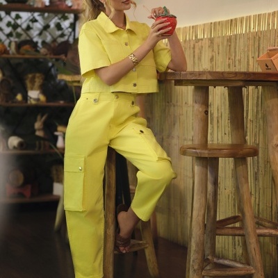 Mulher vestida com conjunto amarelo sentado num banco de madeira com copo em forma de morango.