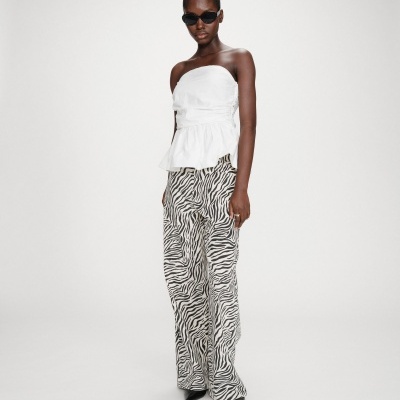 Mulher com top branco e calças com padrão zebra em fundo branco