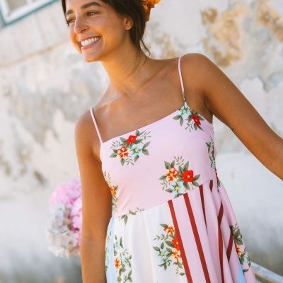 Vestido de mulher com estampa floral e riscas verticais, alças finas e fundo rosa e branco.