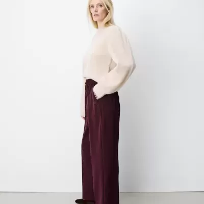 Mulher com camisola bege de malha felpuda e calças largas vinho, em fundo branco