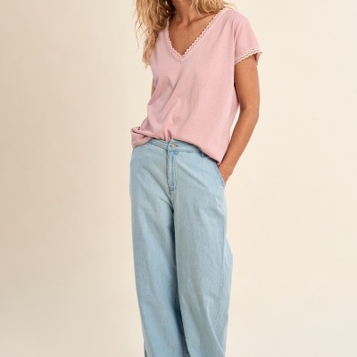 Mulher com t-shirt rosa e calças largas de ganga azuis em fundo neutro