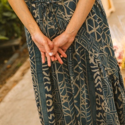 Vestido comprido azul e bege com padrão geométrico e cinto fino, mãos femininas ao centro