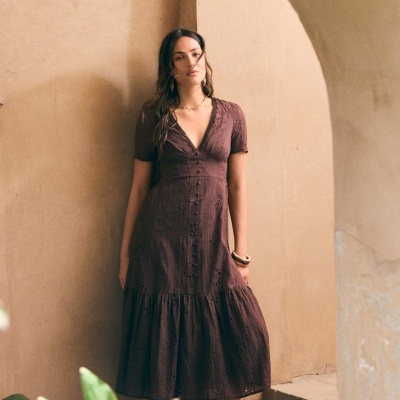 Vestido midi castanho bordado com decote em V e botões, usado por mulher diante de paredes bege.