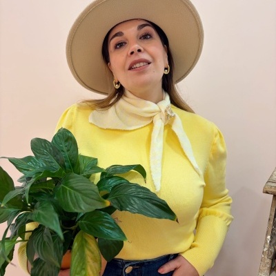 Mulher com camisola amarela, chapéu bege e planta verde
