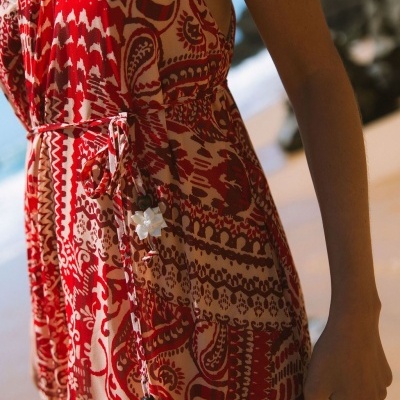 Vestido vermelho e bege com padrão étnico e cinto fino com pendentes de flores brancas.