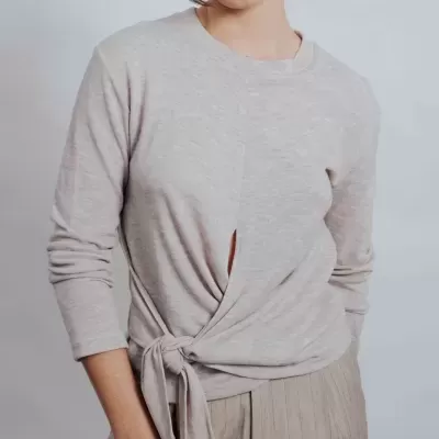 Mulher com camisola cinzento claro com nó frente e calças cinzentas riscada.