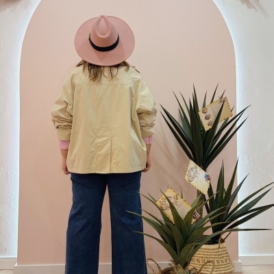 Mulher de costas com camisa bege, calças de ganga, chapéu rosa, plantas em vasos de palha e decoração natural no topo