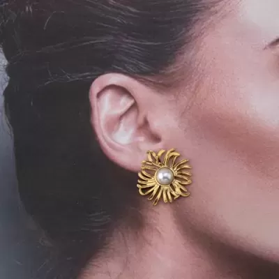 Brinco dourado em forma de flor com pérola no centro, usado na orelha.