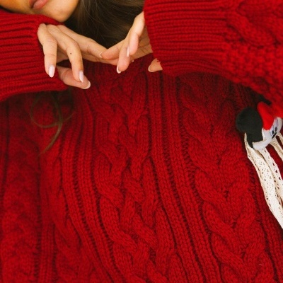 Sweater vermelho de malha grossa com padrão de tranças e pompom decorativo.