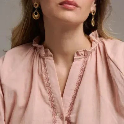 Mulher a usar blusa rosa claro com bordados e brincos dourados