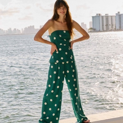 Conjunto verde com bolinhas brancas composto por top e calças largas, usado por mulher junto ao mar.