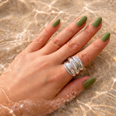 Mão com unhas verdes e anel prateado em areia submersa