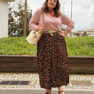 Mulher com camisola rosa, saia animal print, sandálias castanho e mala bege ao ar livre
